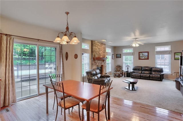 dining space with light wood-style flooring, a chandelier, a fireplace, ceiling fan, and baseboards