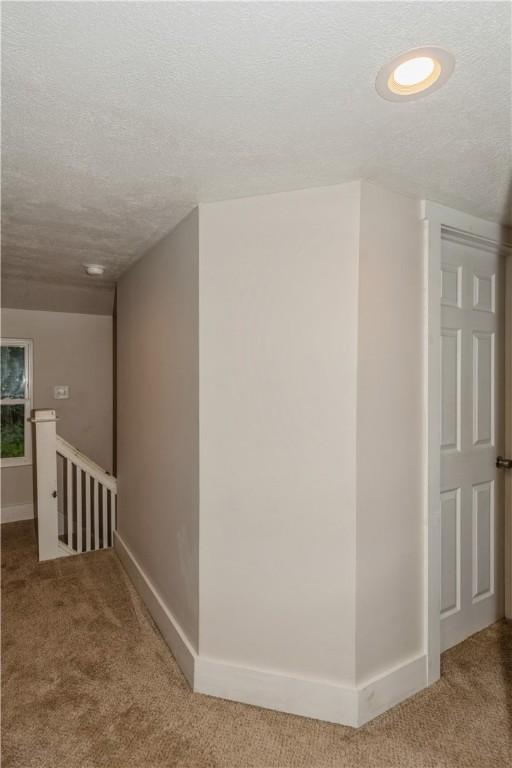hall with carpet floors, an upstairs landing, a textured ceiling, and baseboards