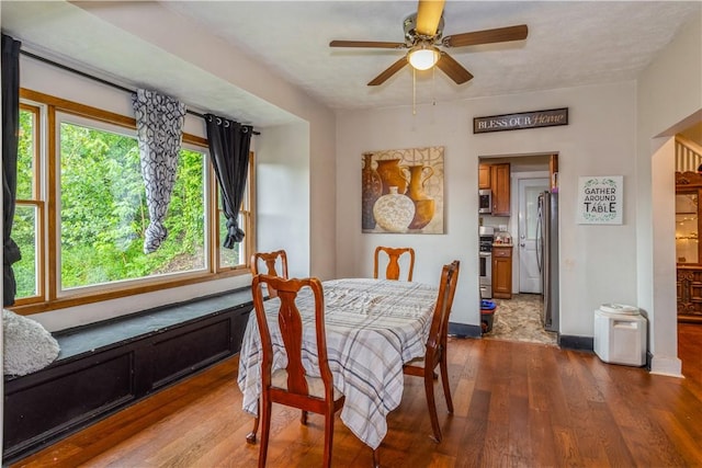 dining room with dark wood finished floors, a ceiling fan, and baseboards