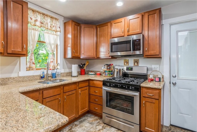 kitchen featuring appliances with stainless steel finishes, a sink, brown cabinets, recessed lighting, and light stone countertops