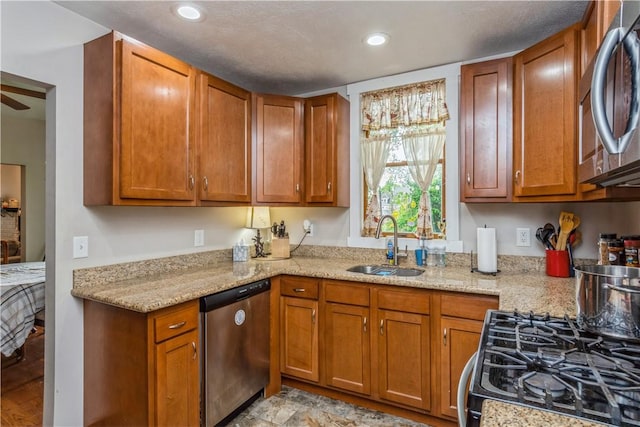 kitchen with stainless steel appliances, a sink, brown cabinetry, light stone countertops, and recessed lighting