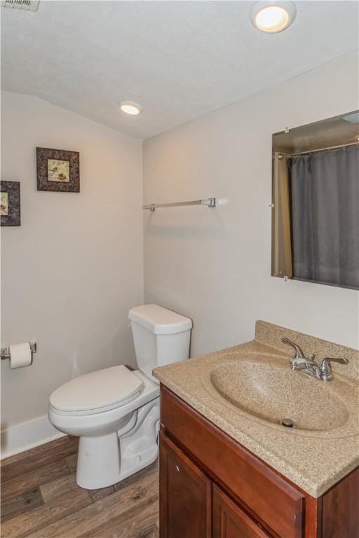 bathroom with toilet, wood finished floors, vanity, baseboards, and lofted ceiling
