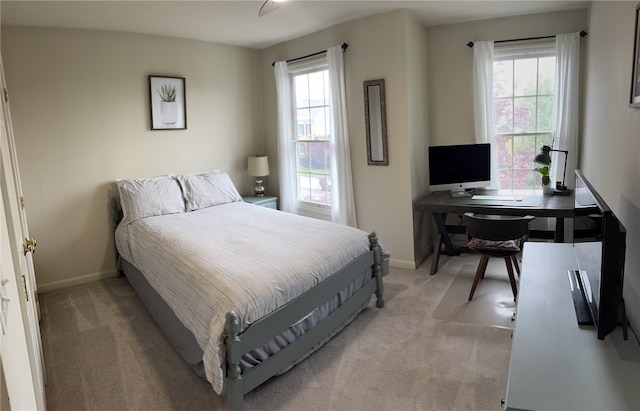 bedroom featuring light colored carpet, multiple windows, a desk, and baseboards