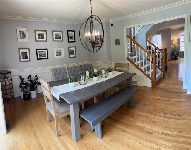dining room with a chandelier, light wood-style flooring, stairs, crown molding, and wainscoting