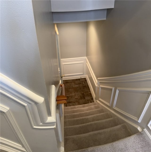 stairway with a decorative wall, a wainscoted wall, and carpet