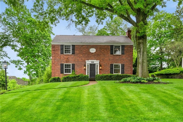 colonial-style house featuring a chimney, a front yard, and brick siding