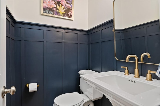 half bathroom featuring a decorative wall, a sink, a wainscoted wall, and toilet