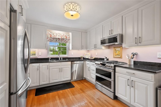 kitchen featuring appliances with stainless steel finishes, white cabinetry, a sink, light wood finished floors, and dark stone countertops