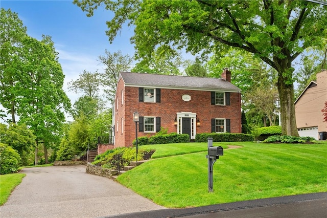 colonial house featuring a chimney, a front yard, and brick siding