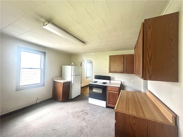 kitchen with electric range oven, freestanding refrigerator, brown cabinets, and light colored carpet