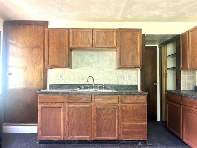 kitchen featuring a sink, dark countertops, decorative backsplash, and brown cabinets