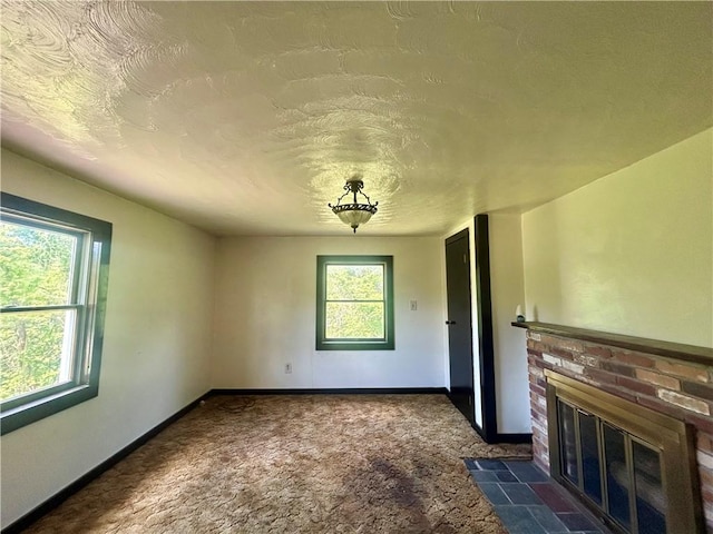unfurnished living room with dark carpet, a brick fireplace, baseboards, and a textured ceiling