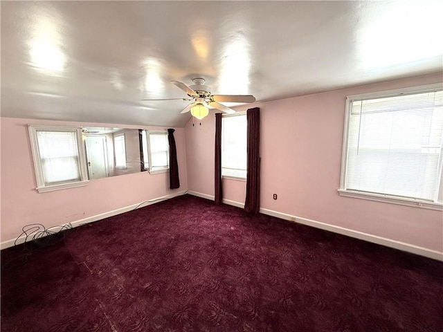 unfurnished room with ceiling fan, baseboards, dark colored carpet, lofted ceiling, and plenty of natural light