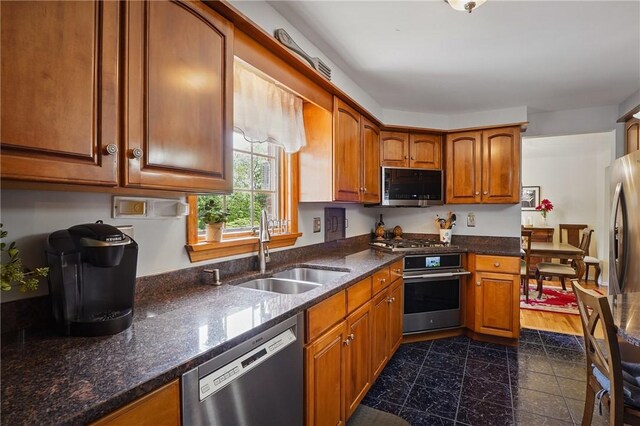 kitchen featuring stainless steel appliances, a sink, brown cabinets, and dark stone countertops