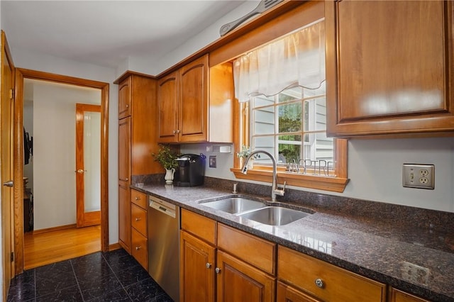 kitchen featuring a sink, dishwasher, brown cabinets, and dark stone countertops