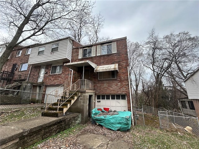rear view of property featuring an attached garage, brick siding, fence, and stairs