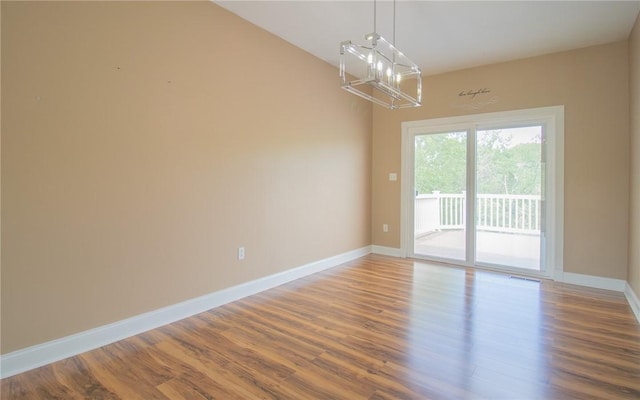 unfurnished room with a chandelier, wood finished floors, and baseboards