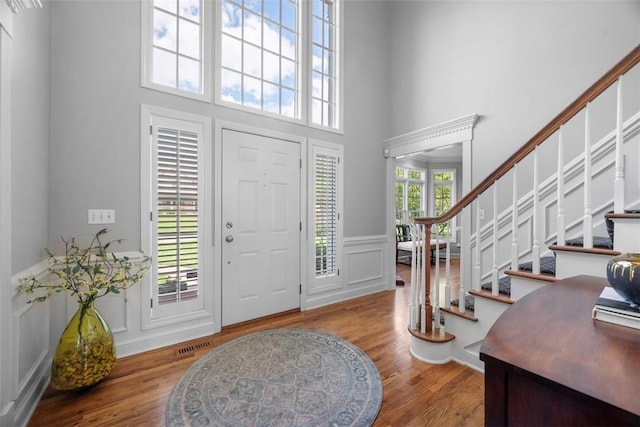 foyer entrance featuring a high ceiling, a decorative wall, stairs, wood finished floors, and a wainscoted wall
