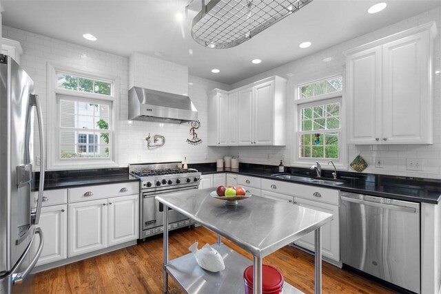 kitchen with appliances with stainless steel finishes, a sink, wall chimney exhaust hood, dark countertops, and recessed lighting