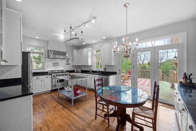kitchen with stainless steel appliances, wall chimney range hood, a sink, dark countertops, and recessed lighting