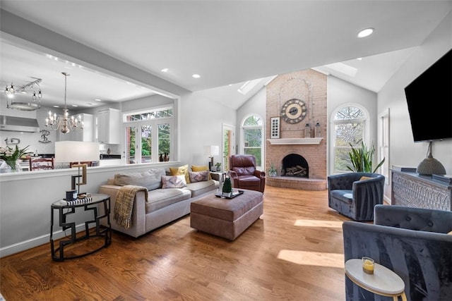 living area featuring a chandelier, wood finished floors, lofted ceiling, a skylight, and a fireplace