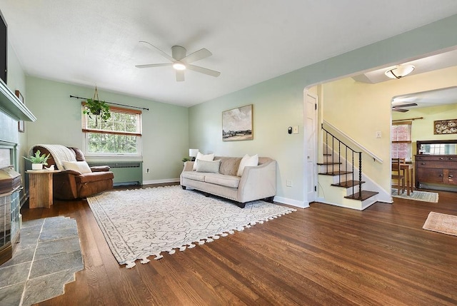 living room with a ceiling fan, wood finished floors, baseboards, and stairs