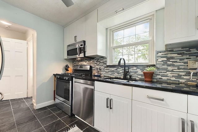 kitchen featuring stainless steel appliances, a sink, dark countertops, decorative backsplash, and white cabinets