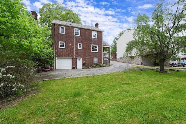 back of house featuring asphalt driveway, a chimney, a garage, and a yard