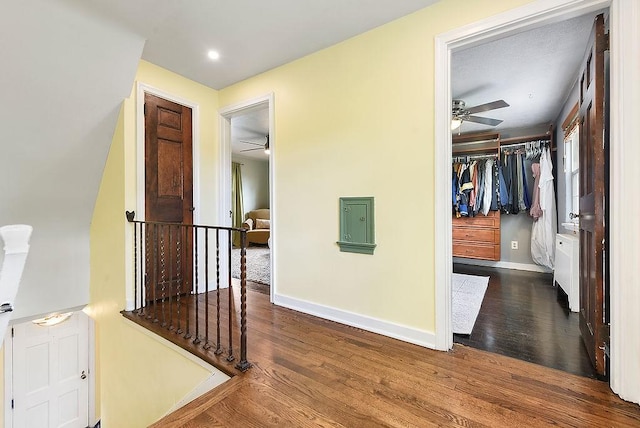 hallway with an upstairs landing, wood finished floors, and baseboards