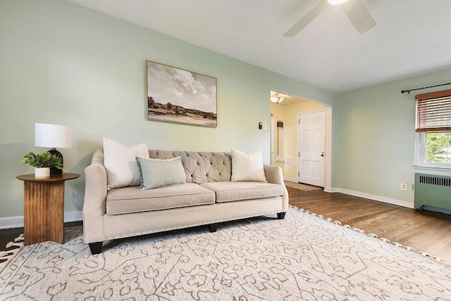 living area featuring radiator, wood finished floors, baseboards, and a ceiling fan