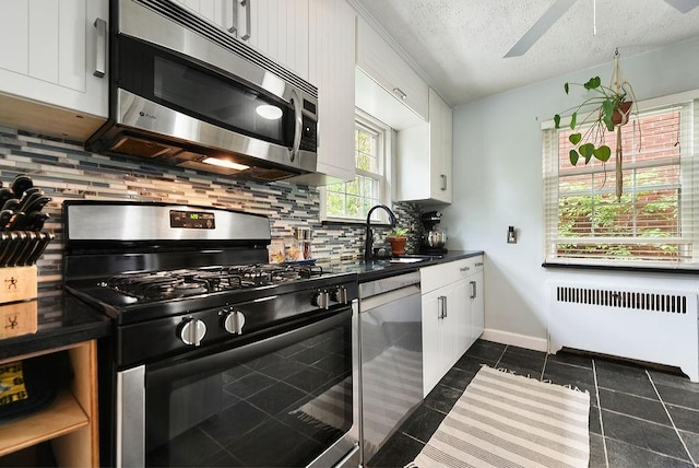 kitchen with appliances with stainless steel finishes, radiator heating unit, a sink, dark countertops, and tasteful backsplash