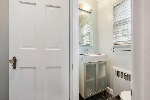 half bathroom with radiator heating unit, vanity, baseboards, and toilet
