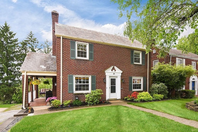 colonial home featuring a chimney, a front lawn, and brick siding