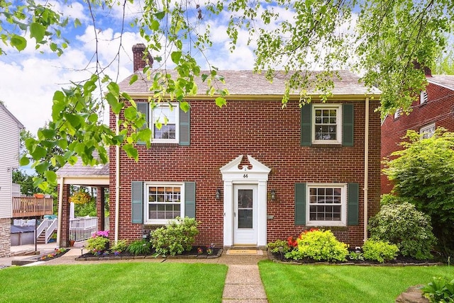 colonial inspired home with a chimney, a front yard, and brick siding