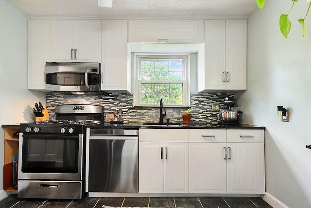 kitchen with stainless steel appliances, a sink, tasteful backsplash, dark countertops, and white cabinetry
