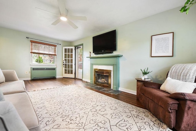 living area featuring radiator heating unit, a tiled fireplace, a ceiling fan, and wood finished floors