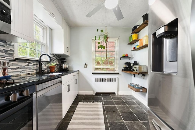 kitchen featuring radiator, appliances with stainless steel finishes, a sink, backsplash, and white cabinets