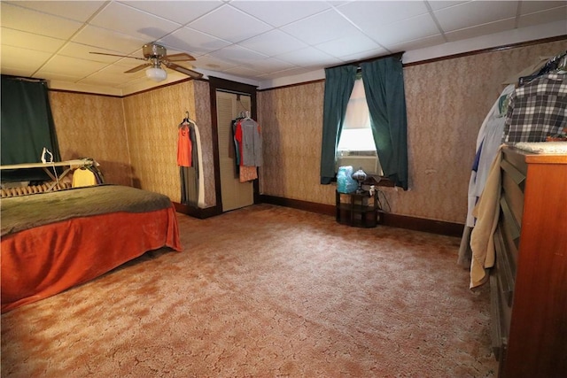 bedroom featuring carpet floors, wooden walls, baseboards, a ceiling fan, and a paneled ceiling