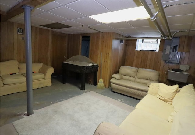 living room featuring wood walls, electric panel, concrete flooring, and a drop ceiling