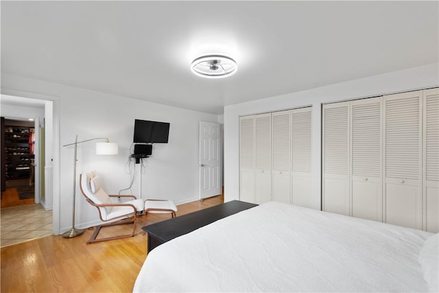 bedroom with two closets, baseboards, and light wood-type flooring
