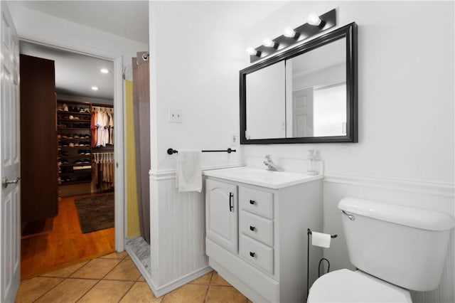 full bathroom with tile patterned flooring, wainscoting, toilet, vanity, and a shower