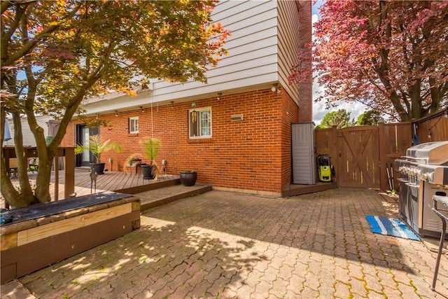 view of patio / terrace featuring a gate, a wooden deck, fence, and a grill