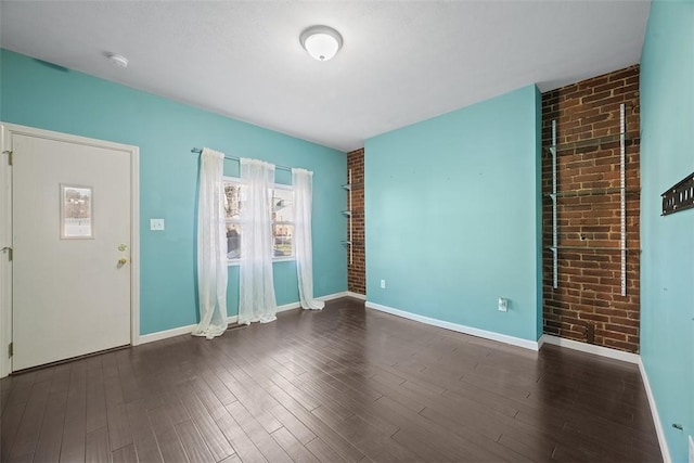 empty room with brick wall, wood finished floors, baseboards, and a smoke detector