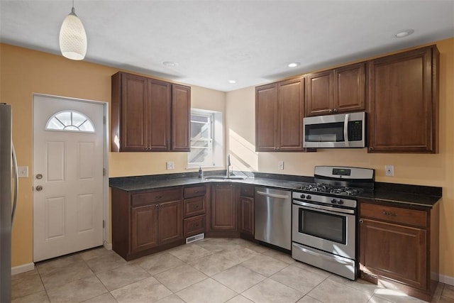 kitchen with appliances with stainless steel finishes, a sink, dark countertops, recessed lighting, and light tile patterned floors
