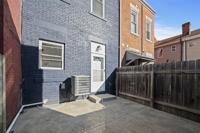 back of property with fence, central AC unit, brick siding, and a patio