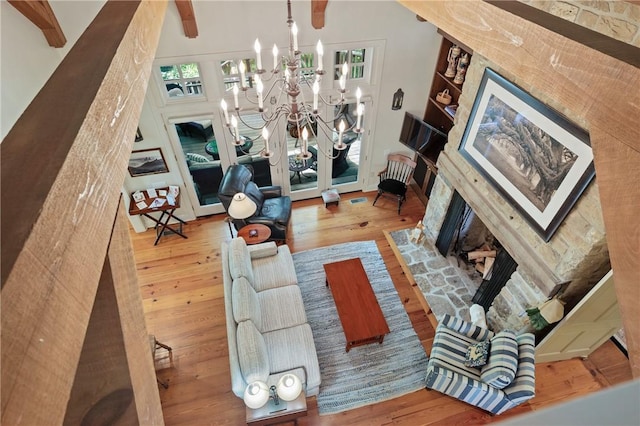 living area with wood finished floors, a chandelier, a fireplace with flush hearth, plenty of natural light, and a towering ceiling