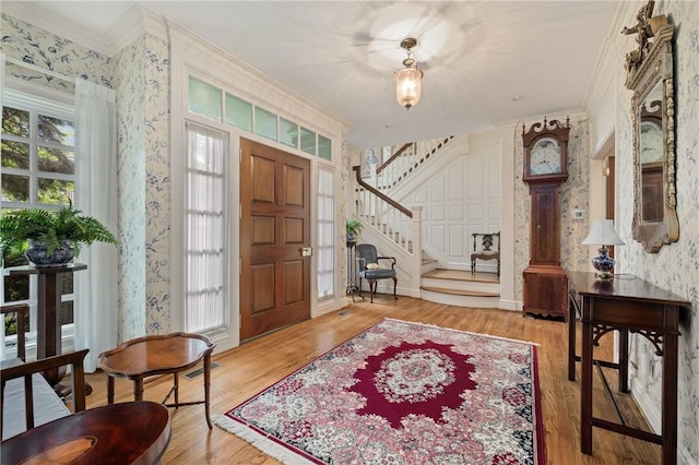 entrance foyer with ornamental molding, stairs, wood finished floors, and wallpapered walls