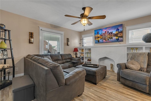 living area featuring light wood-style floors, ceiling fan, and a fireplace