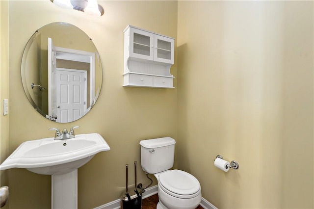 half bath featuring toilet, baseboards, and a sink