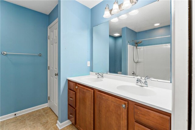 bathroom featuring baseboards, a shower, double vanity, and tile patterned floors
